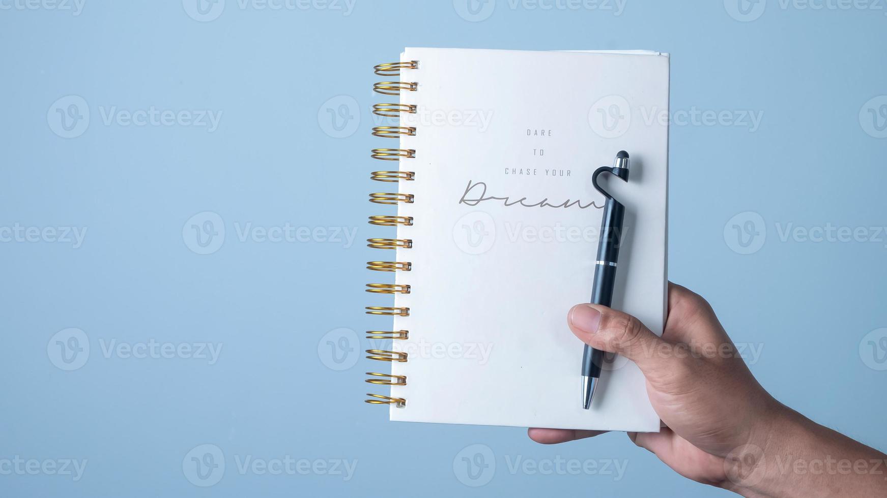 Hand holding a pen and note book on blue background, business concept photo