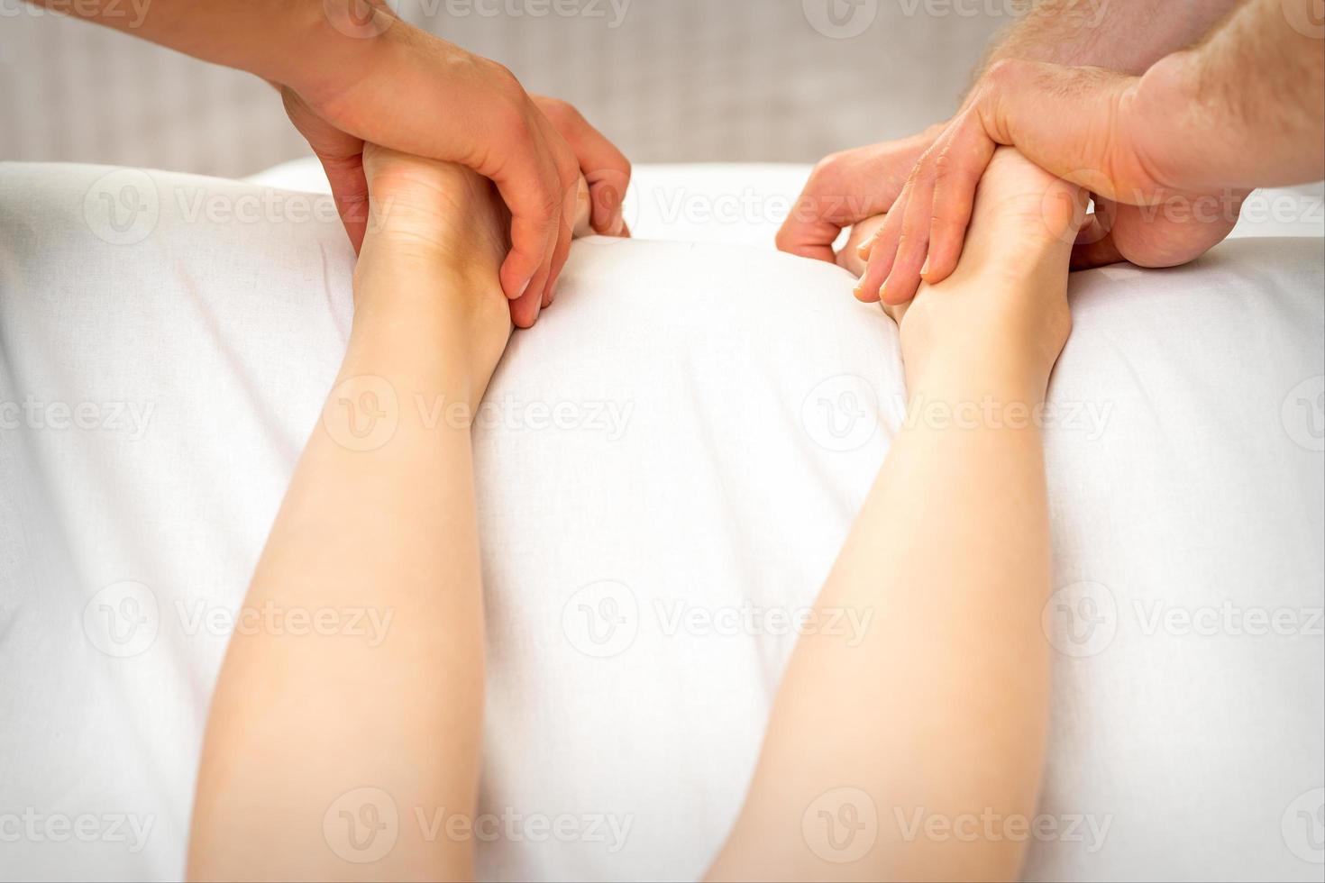 Two masseurs massaging feet of woman photo