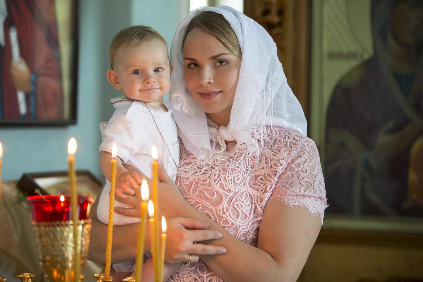 ortodoxo bautismo. madre y niño en un Iglesia por luz de una vela. mujer con un bebé en el templo. foto