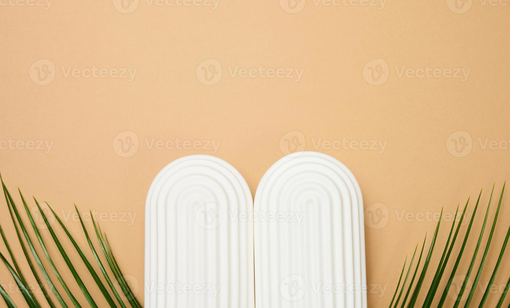Green palm leaves and white decorative arches on a brown background, a stage for product display, cosmetics photo