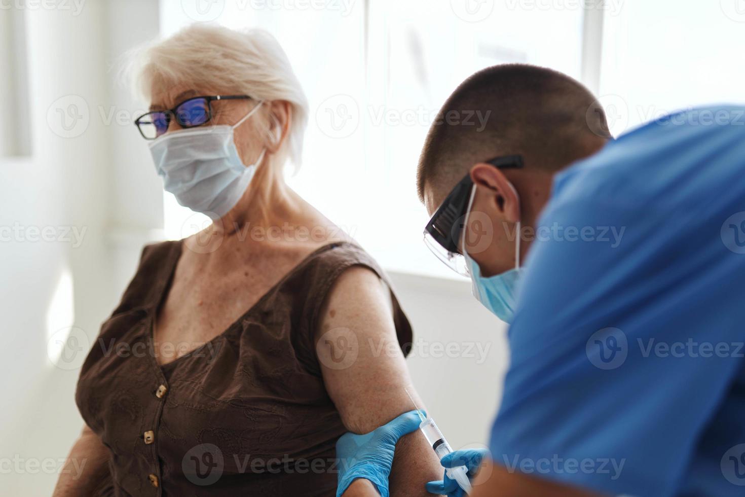 médico dando un inyección a el mano de un mayor mujer paciente con un codicioso pasaporte foto