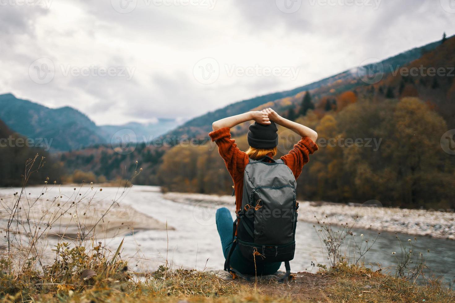 woman traveler with a backpack on her back gestures with her hands and looks at the mountains in the distance photo