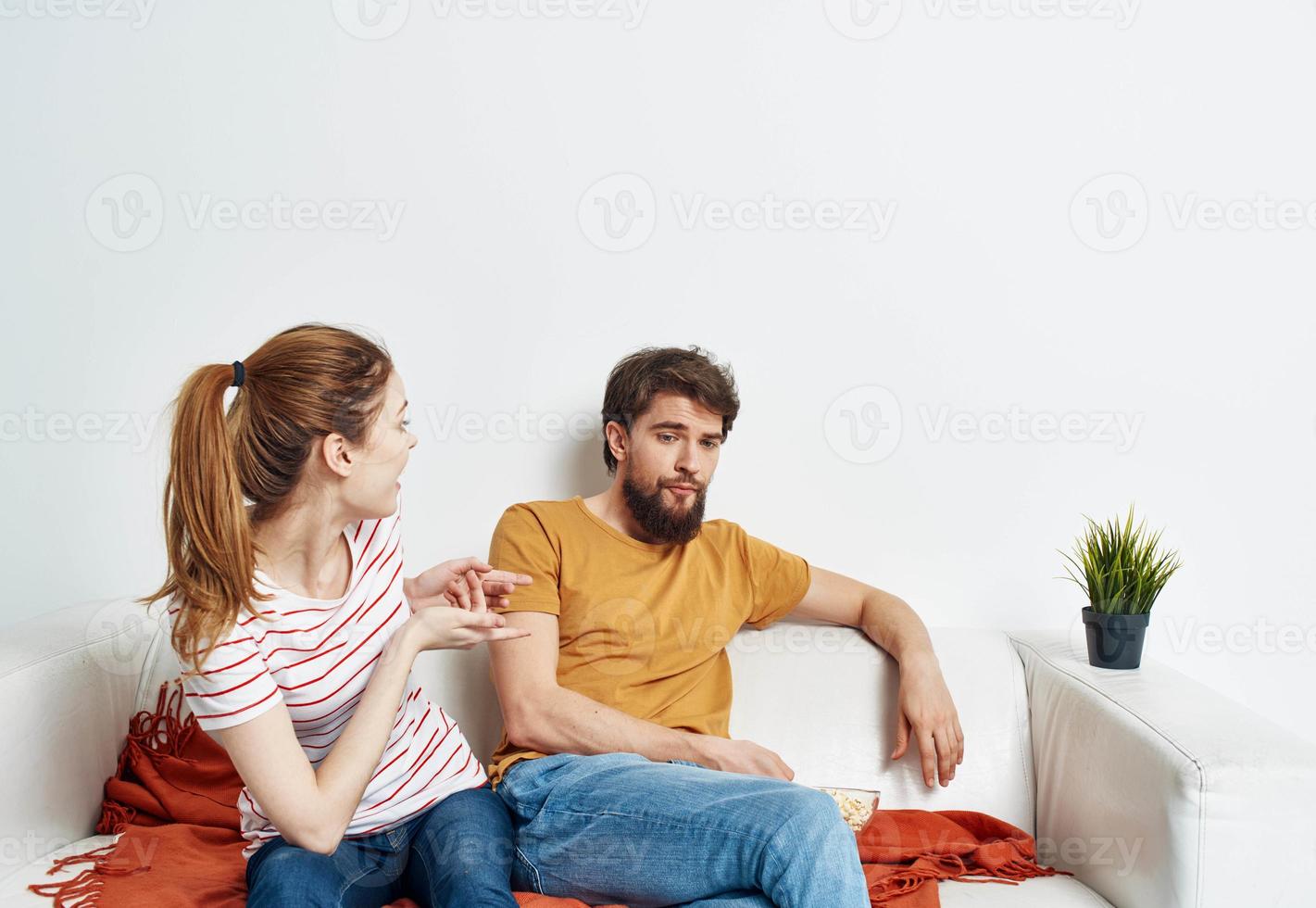 A man with popcorn in a plate and a woman are sitting on the couch watching TV and watching movies photo