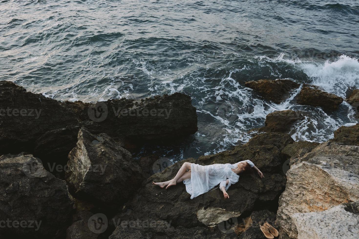 hermosa mujer en un blanco vestir acostado en un Roca en un blanco vestir ver desde encima foto