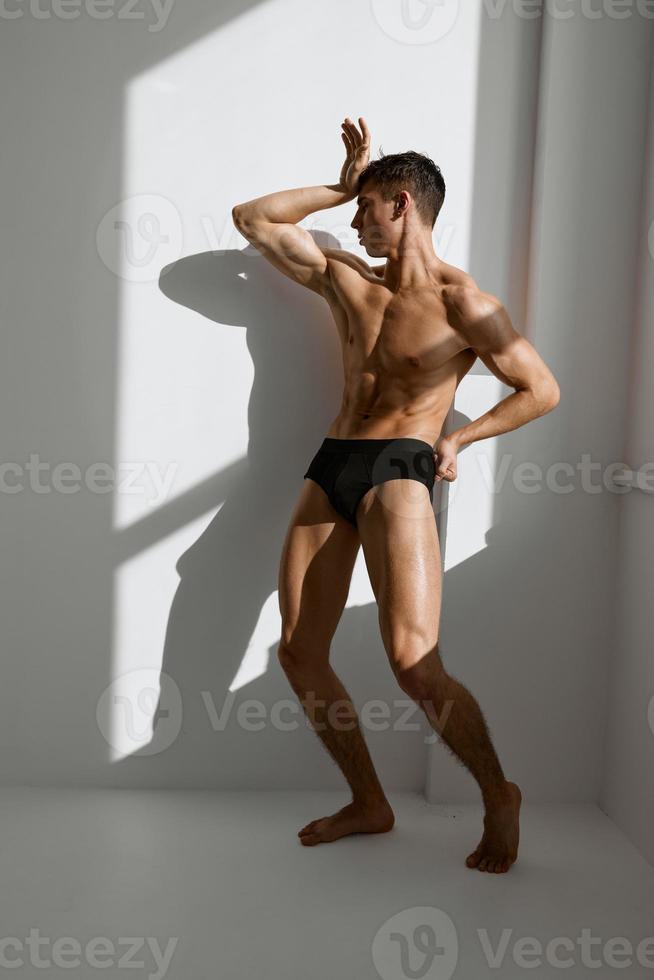 sporty man with pumped up naked body in black panties posing near the window photo