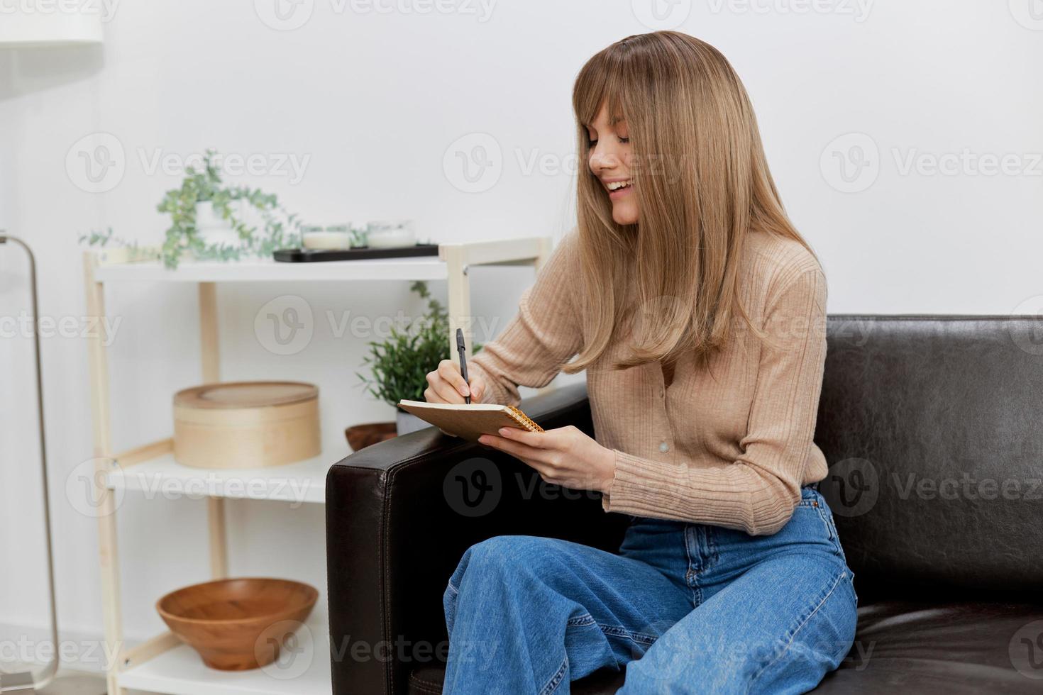 Focused cheerful blonde student lady with copybook enjoy cool task sitting in sofa couch at modern living room interior. Female client have shrink appointment in psychological help office. Copy space photo