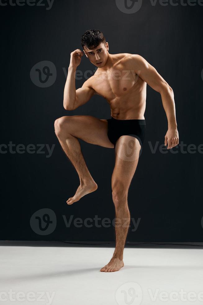 hombre con un muscular cuerpo en negro pantalones cortos posando oscuro antecedentes foto
