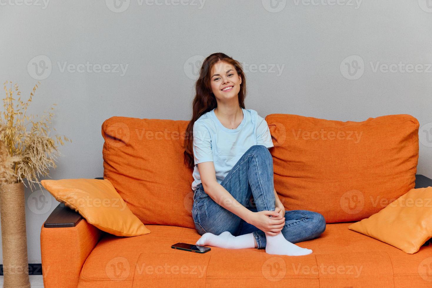 cheerful woman sits on an orange sofa with a phone photo