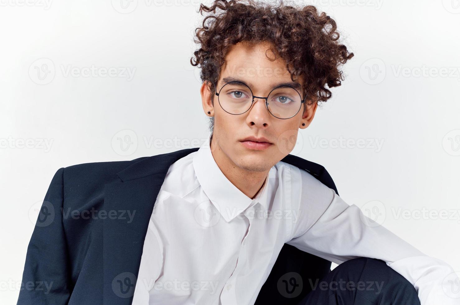 portrait of a curly-haired guy in a shirt in a jacket and glasses on a light background close-up photo