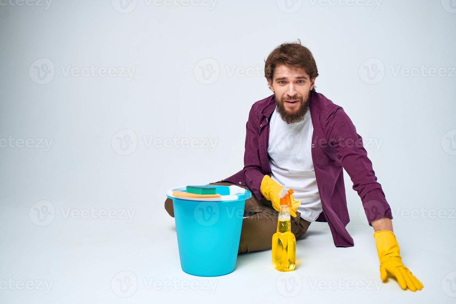 A man lies on the floor with a bucket of detergent cleaning service light background photo