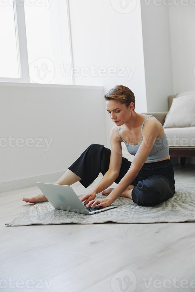 Freelance woman with laptop and phone works from home sitting on the floor in her home clothes with a short haircut, free copy space photo