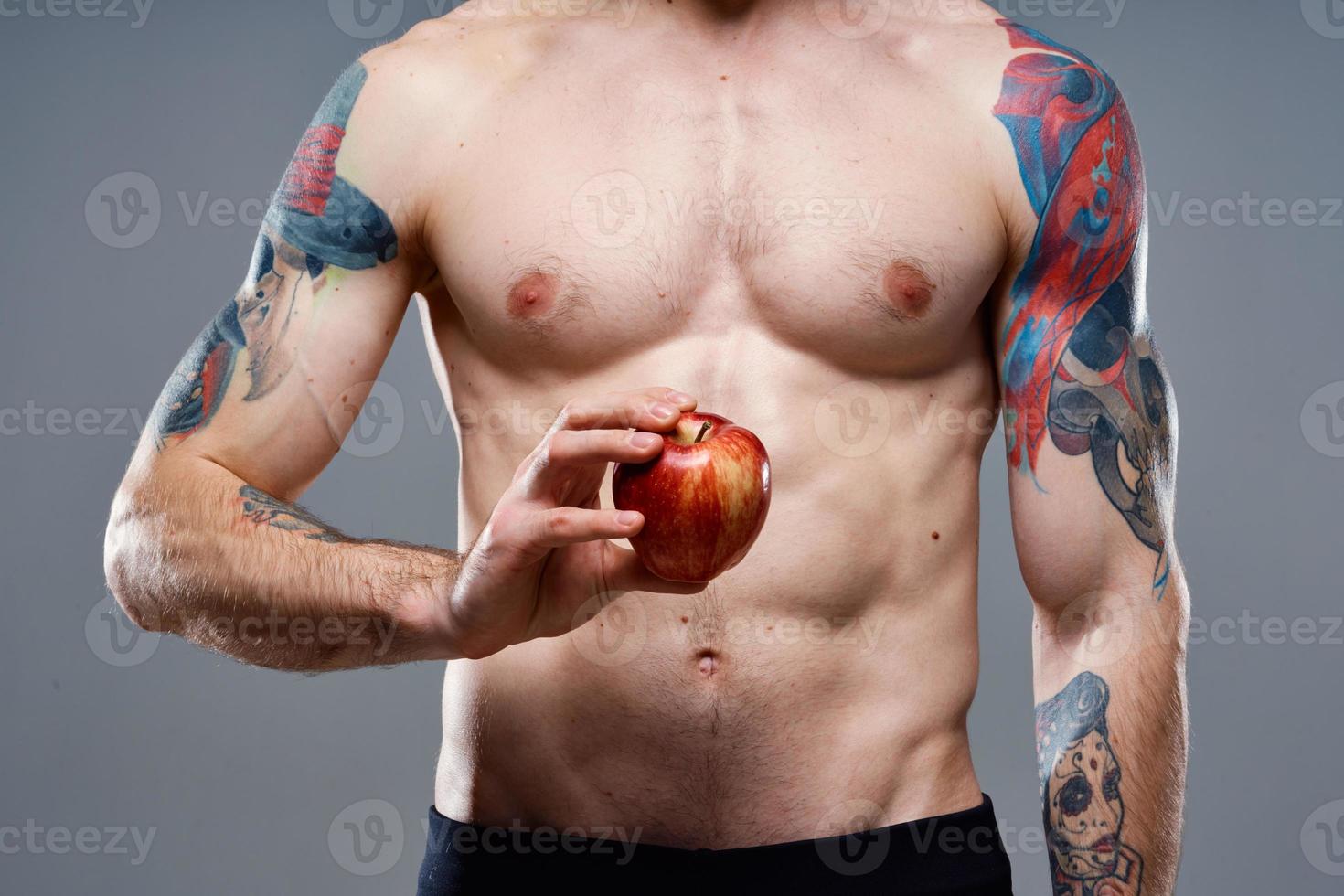 young man with apple and pumped up torso biceps man tattoo gray background cropped view photo