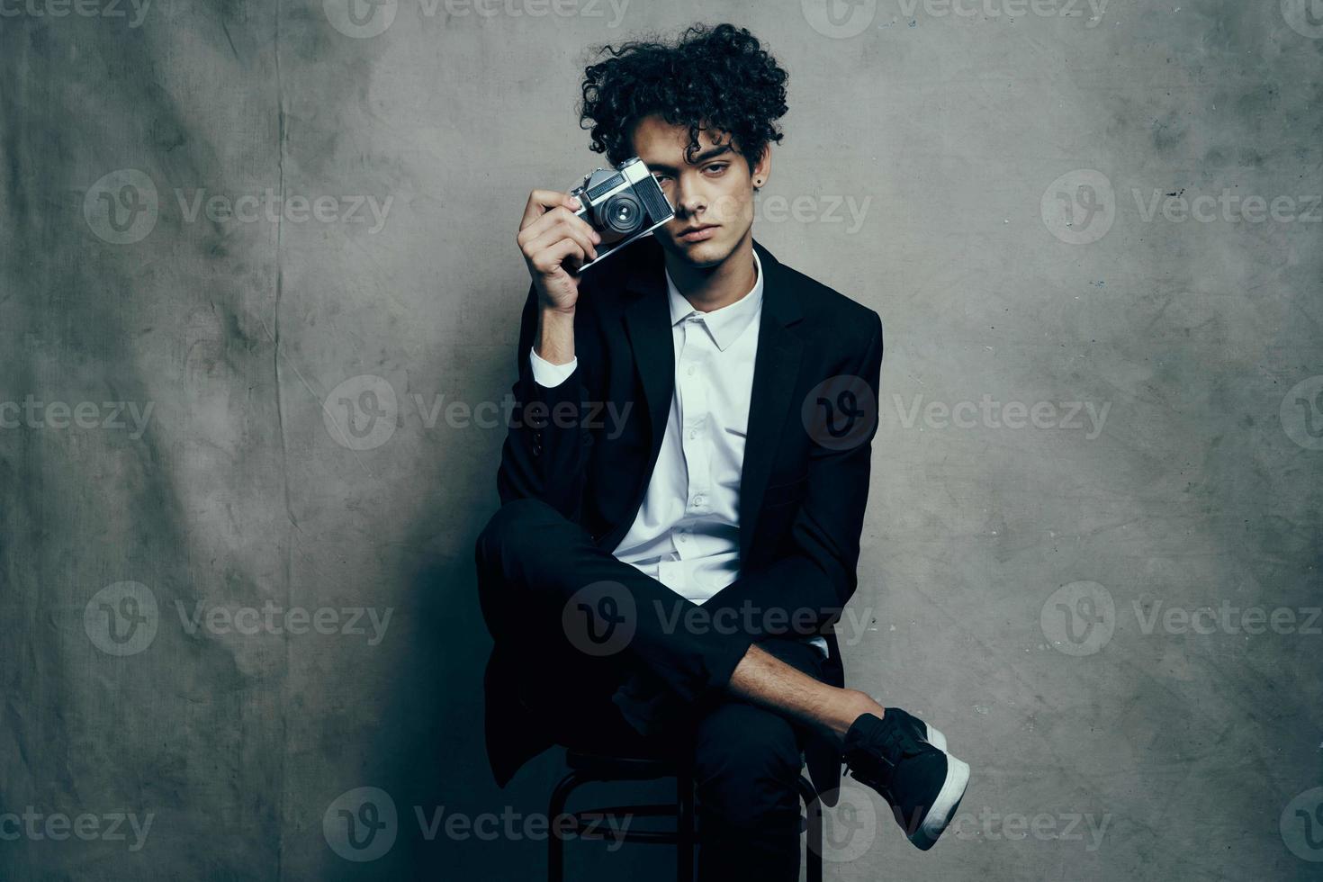 a man in a suit with a camera in his hands sits on a chair and chairs photo
