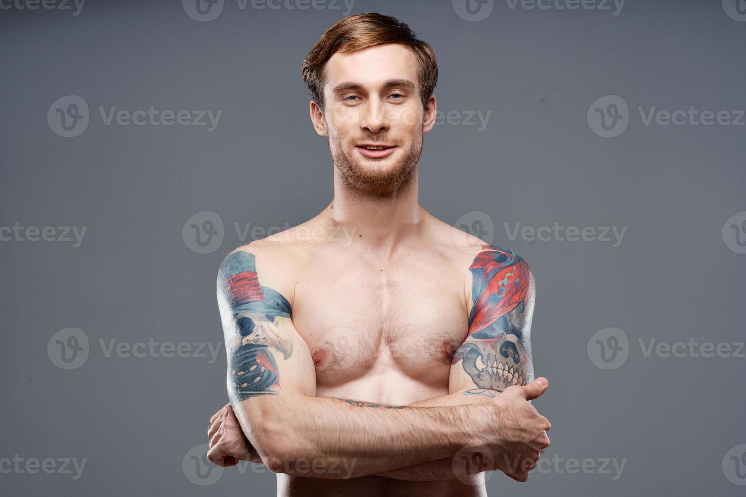 sexy bodybuilder with naked torso made of muscle tattoos gray background crossed arms on chest photo