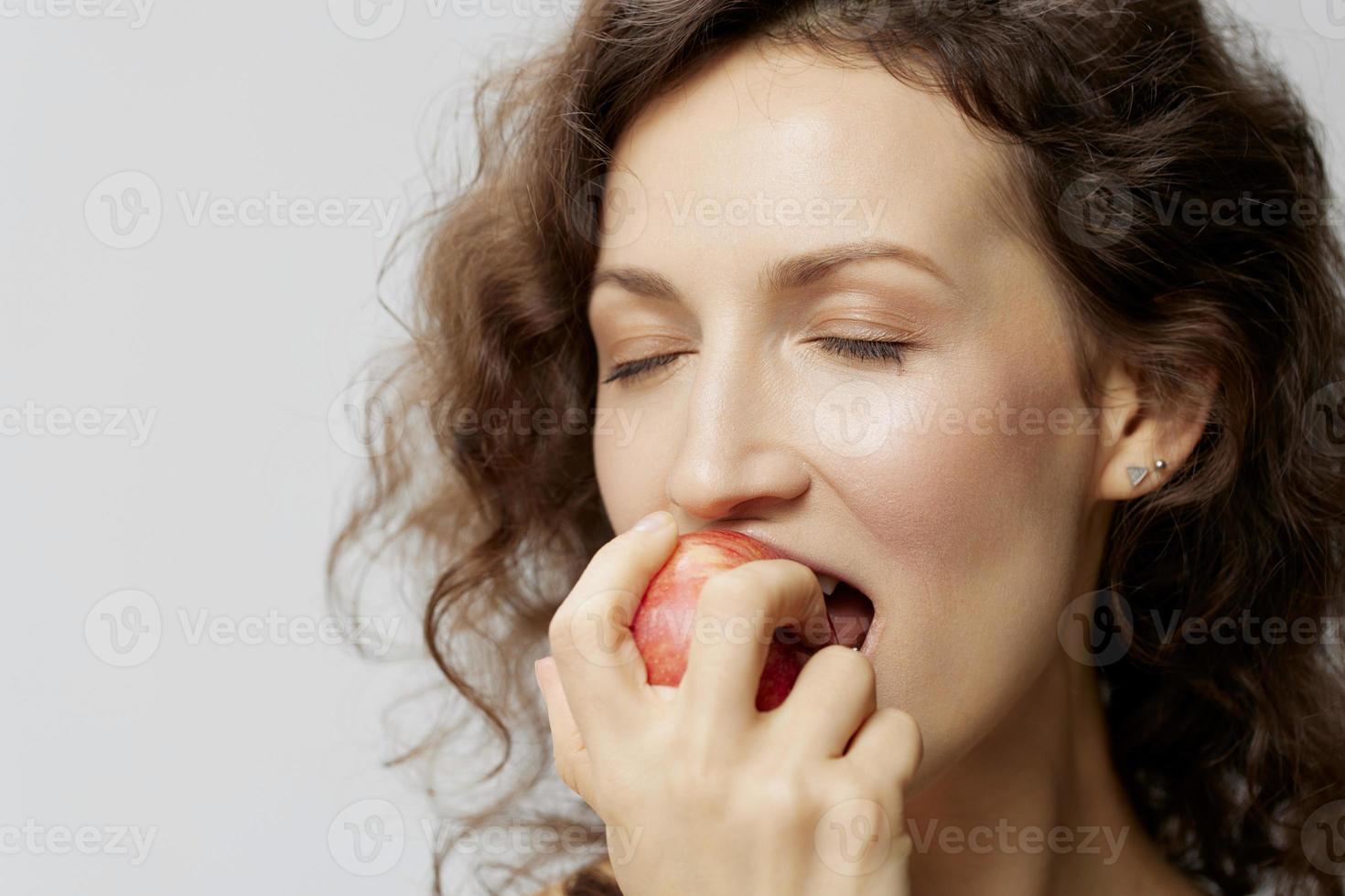 Closeup portrait of happy curly beautiful woman in basic white t-shirt enjoy fresh apple fruit posing isolated on over white background. Natural Eco-friendly products concept. Copy space photo