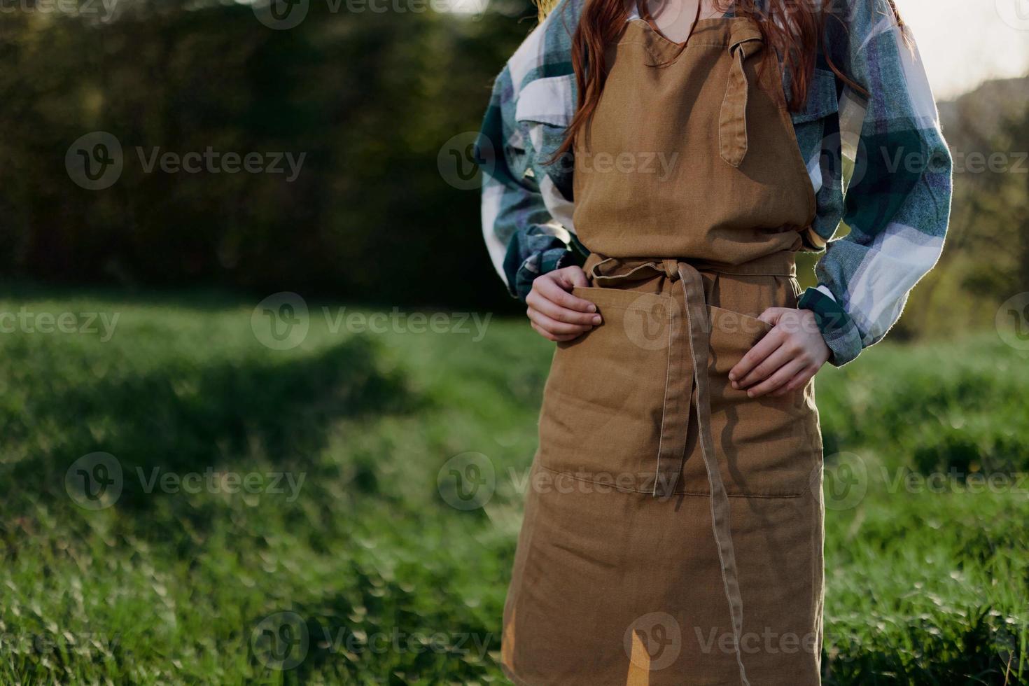 Close-up of a woman in a gardener's work apron against the green, fresh summer grass outdoors showing her hands photo