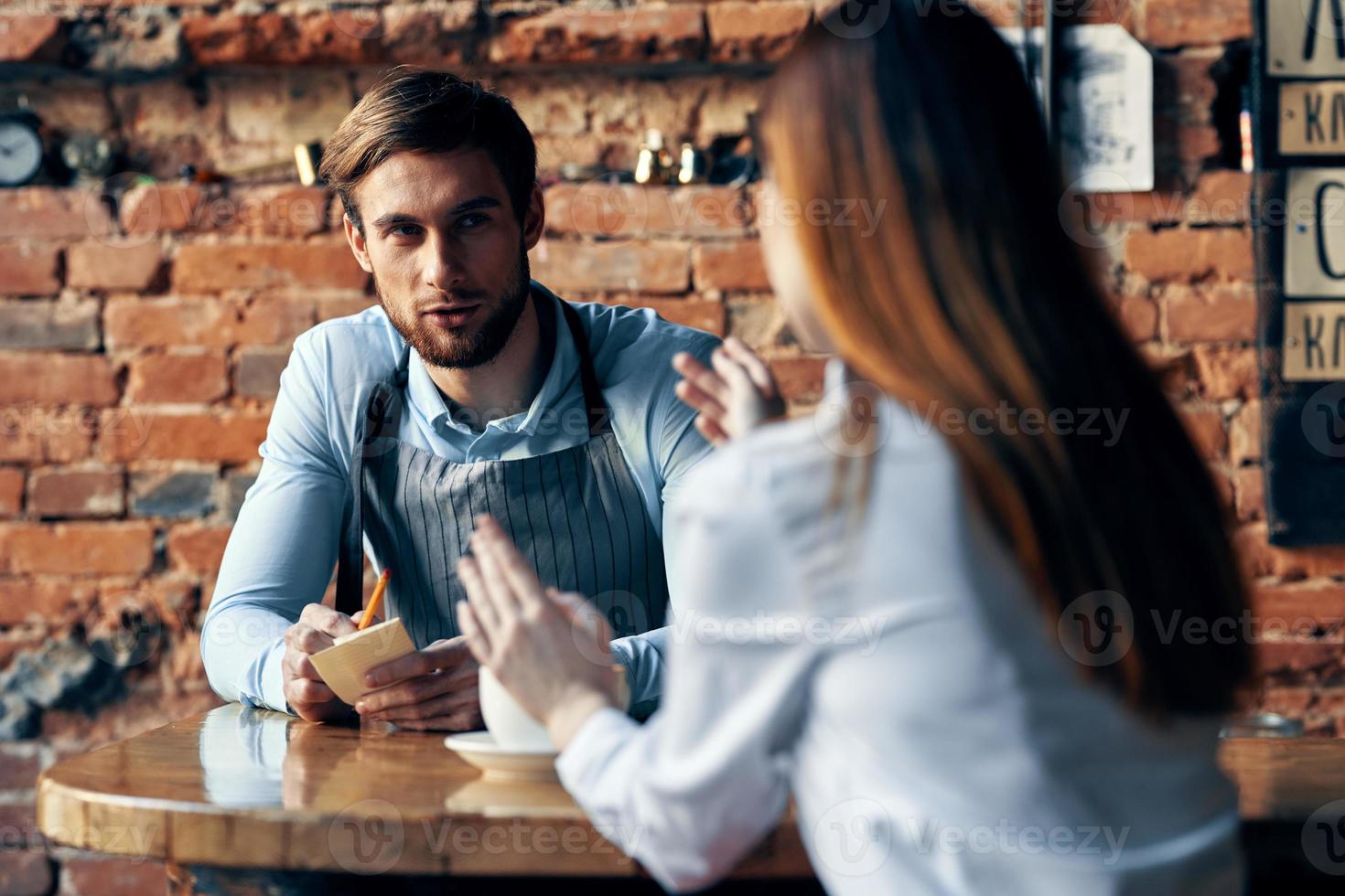 a man with a cup of coffee and all aprons at a cafe table and a woman in a shirt and red skirt cropped view photo