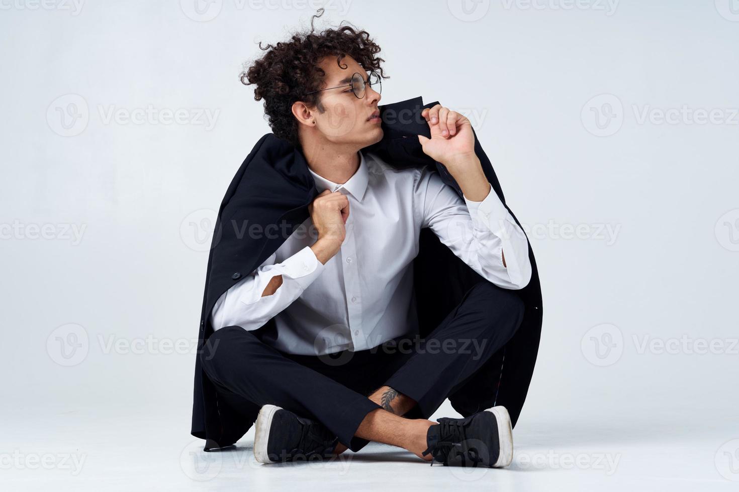 curly-haired guy straightens his jacket over his shoulders and sits on the floor in sneakers and in a suit photo