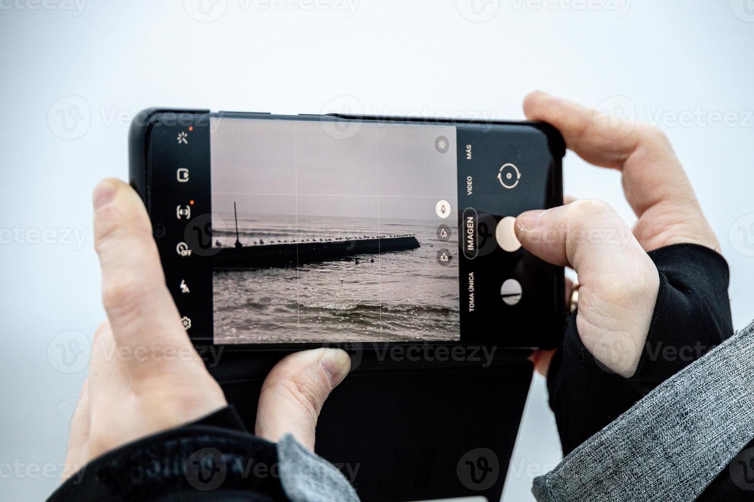 on the phone while taking a picture at the Baltic Sea on winter day photo