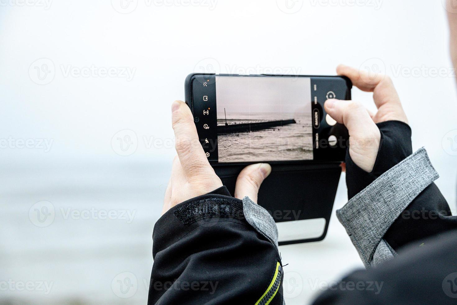 on the phone while taking a picture at the Baltic Sea on winter day photo