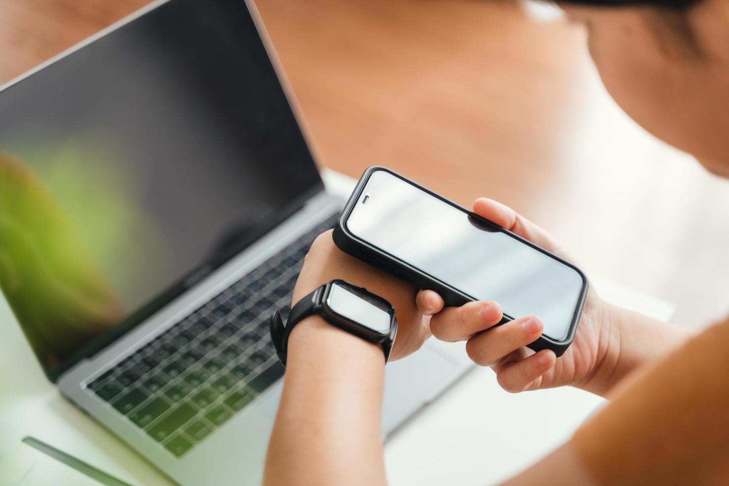 Woman use smartphone and smartwatch for tracking activity on sofa in living room at home, wireless connection between the watch and mobile phone. photo