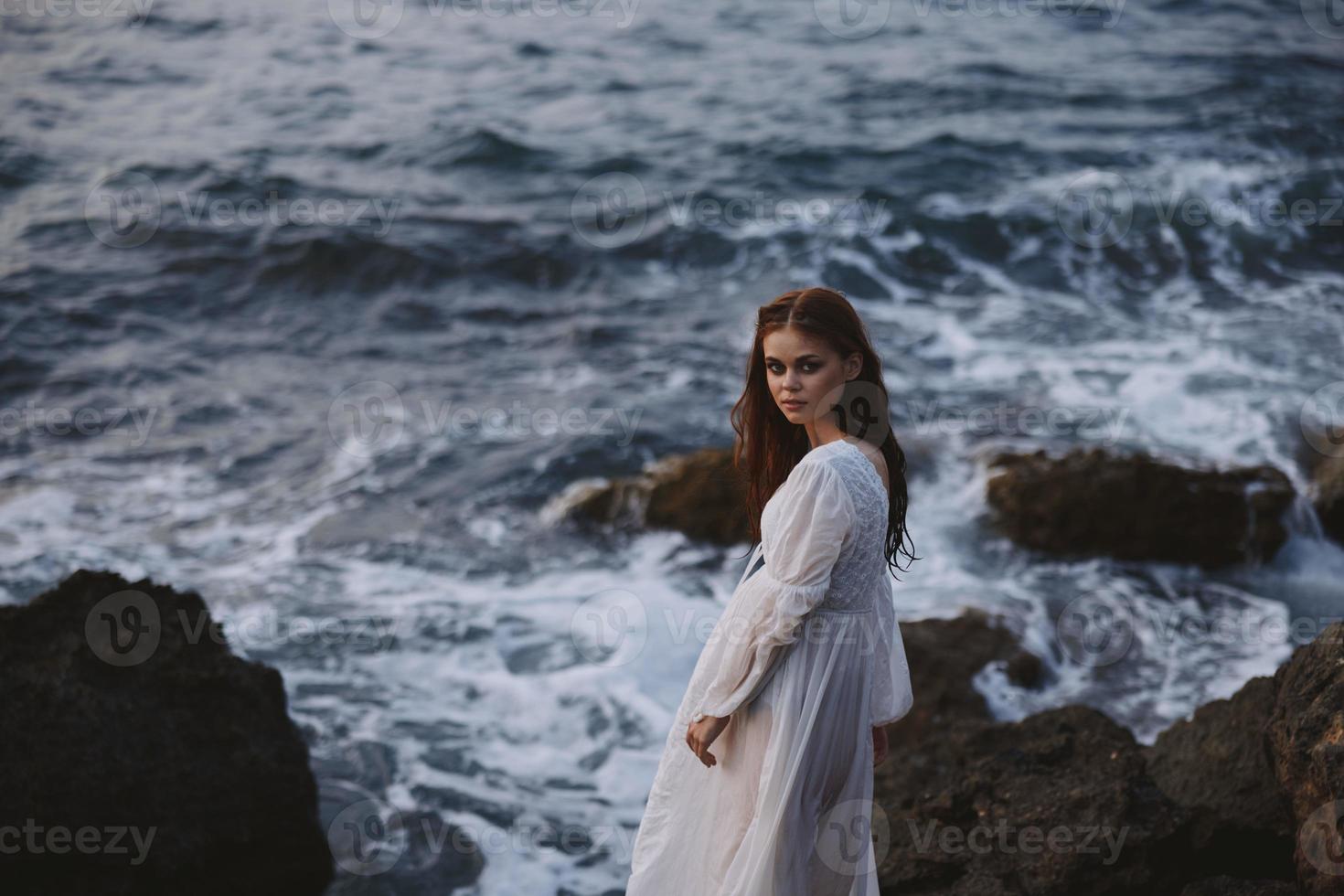 mujer en blanco vestir soportes en un acantilado estilo de vida Roca costa paisaje inalterado foto