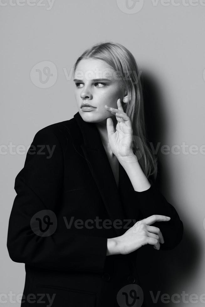 Elegant girl puts her hand to her face tucks her hair behind her ear poses in the studio in black and white style photo