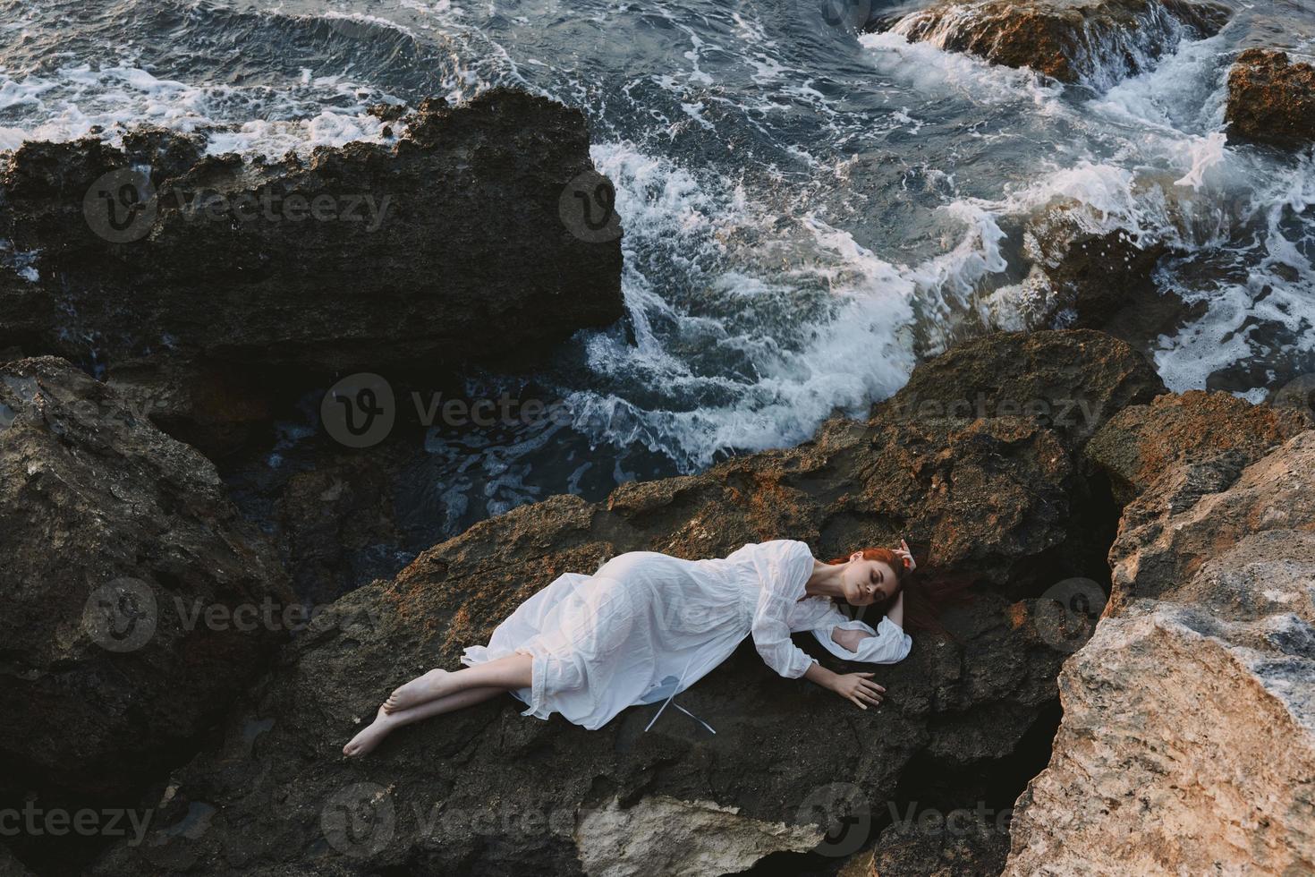 hermosa joven mujer en un aislado Mancha en un salvaje rocoso costa en un blanco vestir paisaje foto