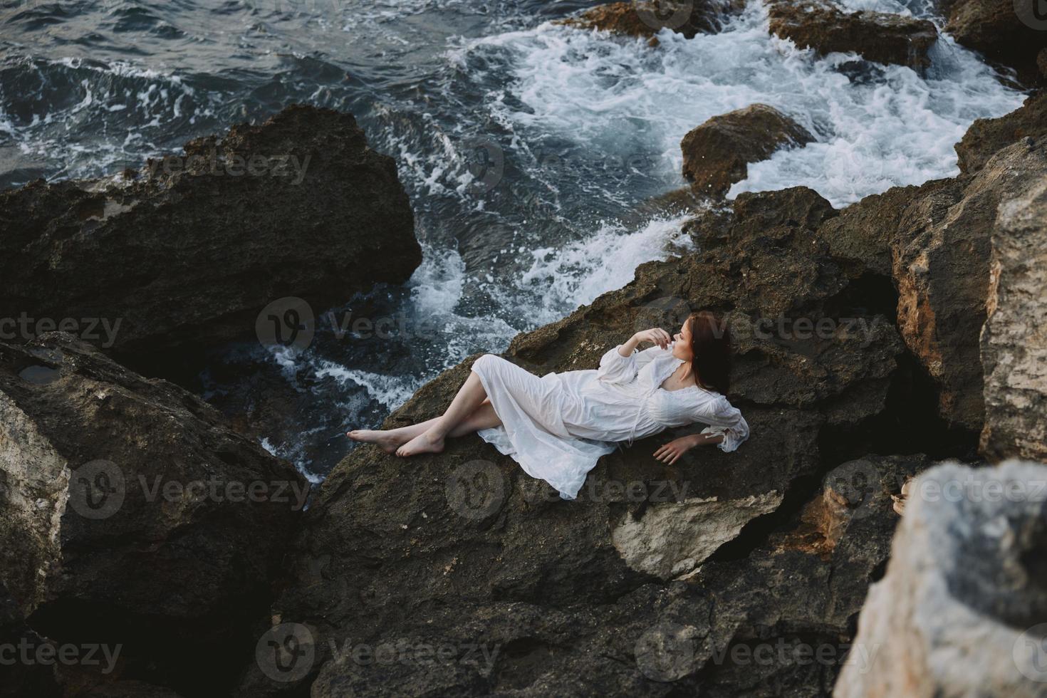 hermosa mujer en un aislado Mancha en un salvaje rocoso costa en un blanco vestir inalterado foto