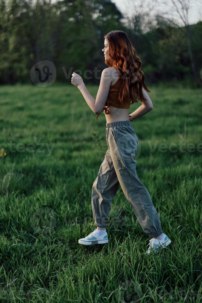 un joven mujer hacer ejercicio fuera de y corriendo en el parque. en el noche en el verde césped dentro el puesta de sol foto