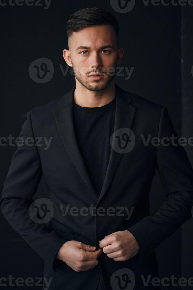 Modelling snapshots. Narcissistic self-confident tanned attractive handsome man in classic suit jacket looks at camera posing isolated in over black studio background. Fashion offer. Copy space for ad photo