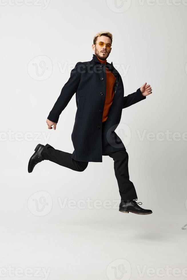 a blond man in a coat jumped up and runs to the side on a light background photo