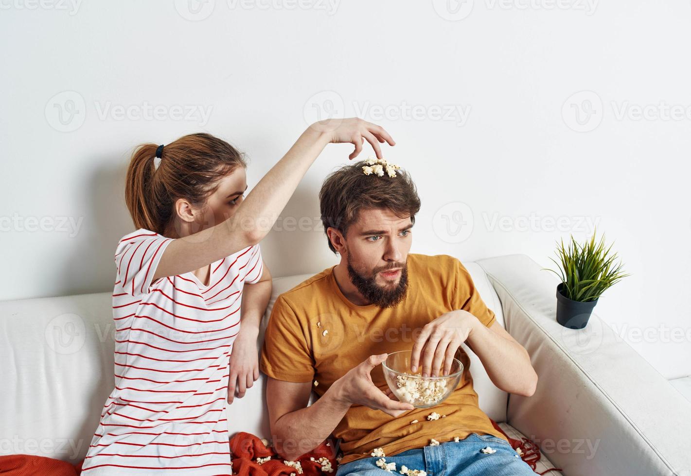 A woman in a striped T-shirt and a man on the couch watching the TV in a bright room photo