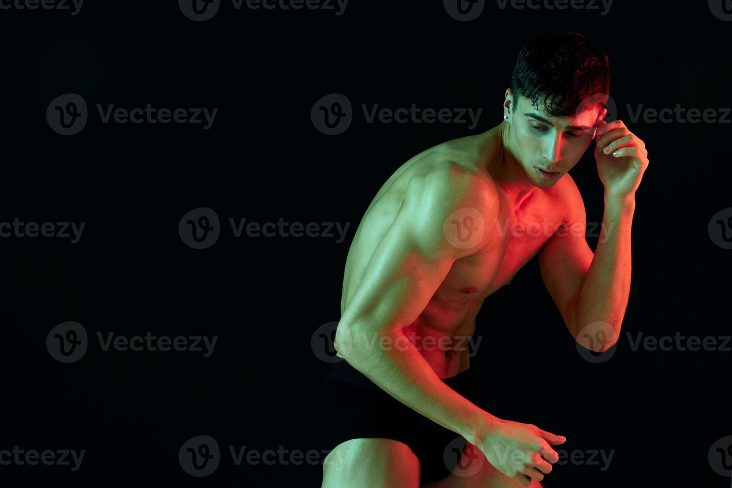 man in shorts posing on a black background with a pumped-up torso biceps fitness photo