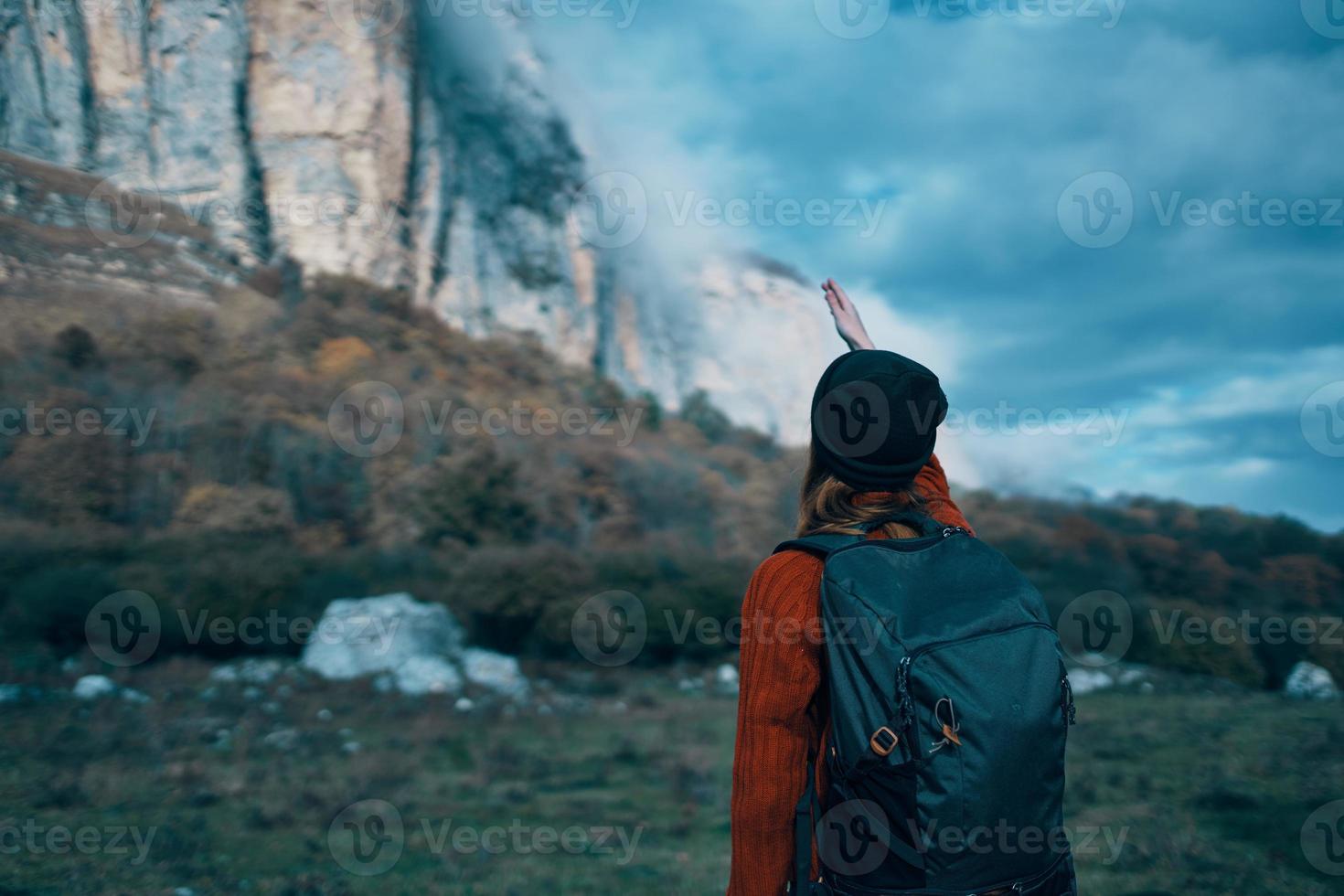 a traveler with a backpack and in a red sweater shows the mountains with her hand and the blue sky clouds photo