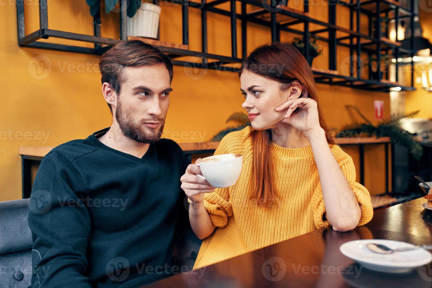 romántico mujer abrazos un joven hombre en un suéter a un mesa en un café interior un Pareja en amor foto