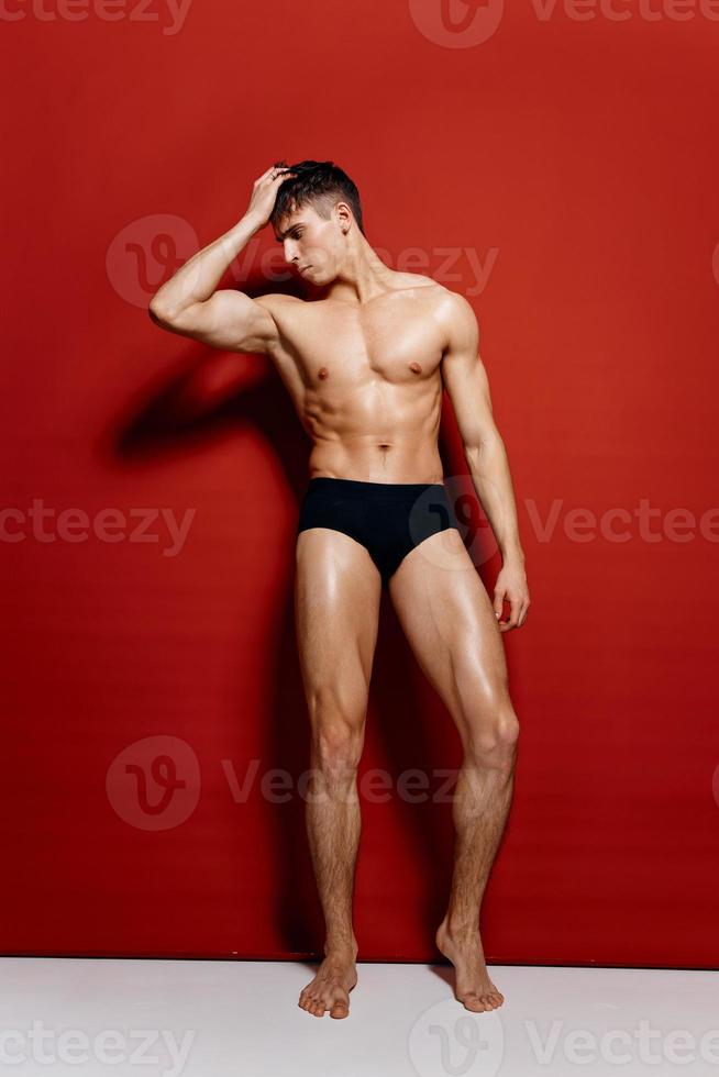 guy with pumped up arm muscles pagebuilder in black panties in full growth on a red background photo