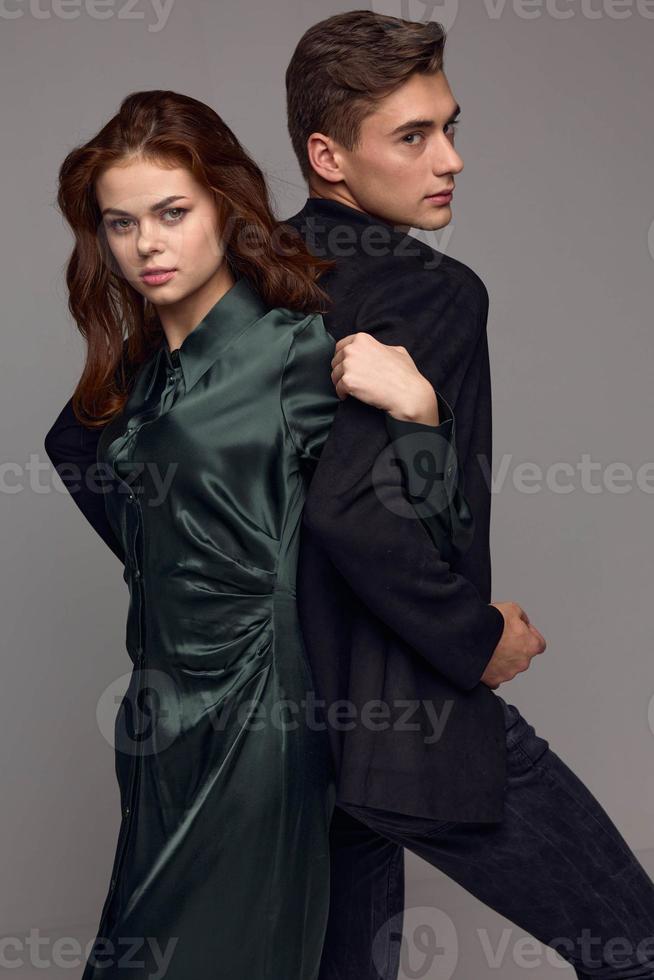 A man in a classic suit and a woman in a dress on a gray background stand with their backs to each other photo
