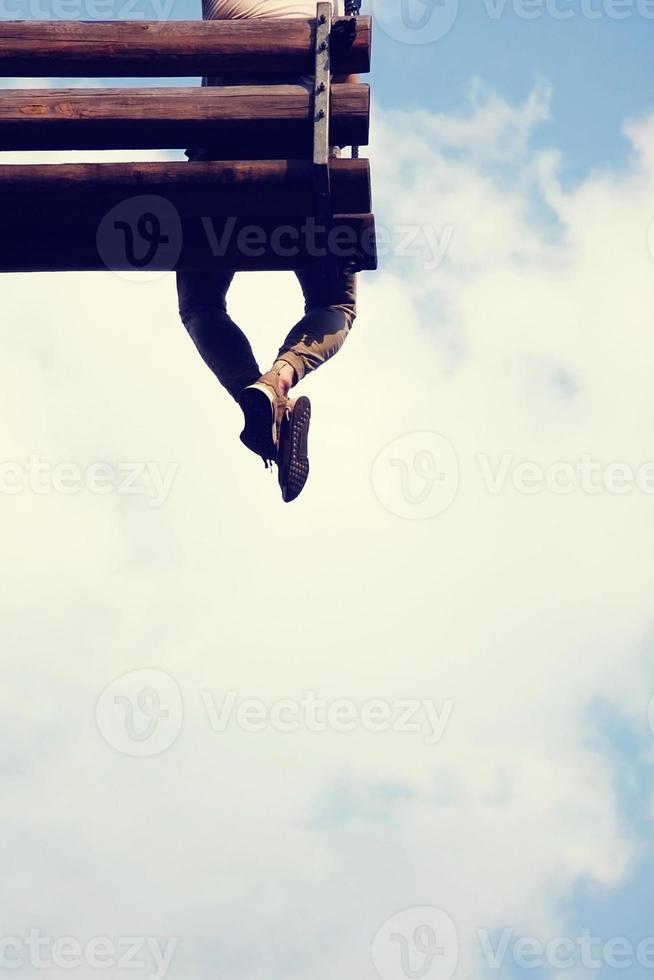 One young man sitting on wooden swing in the sky with his legs crossed. Back view, copy space. photo