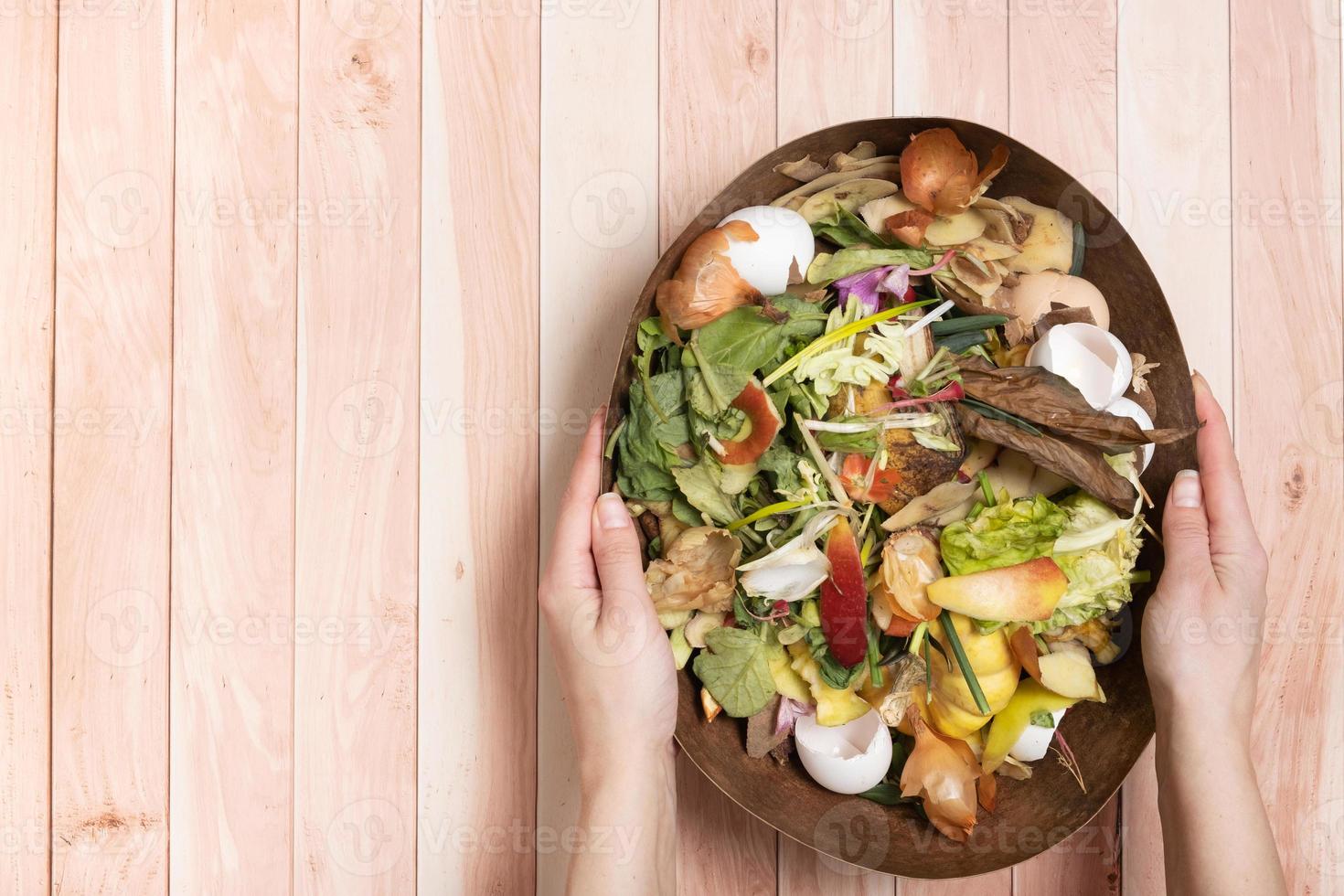 Organic garbage for compost in female hands on a wooden background. Composting concept flat lay, top view photo