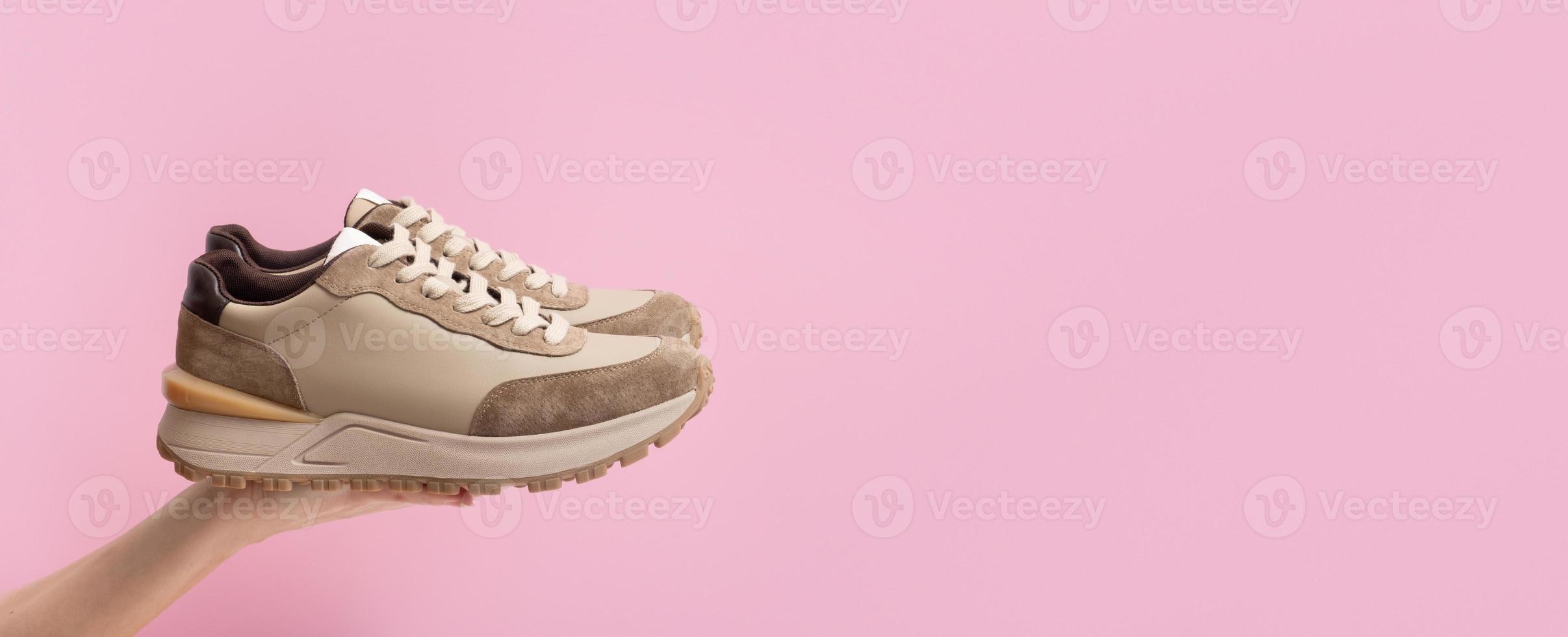 Beige women's leather sneakers in hand on pink background photo