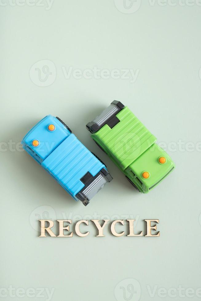 Two toy garbage trucks and recycle text on a green background photo