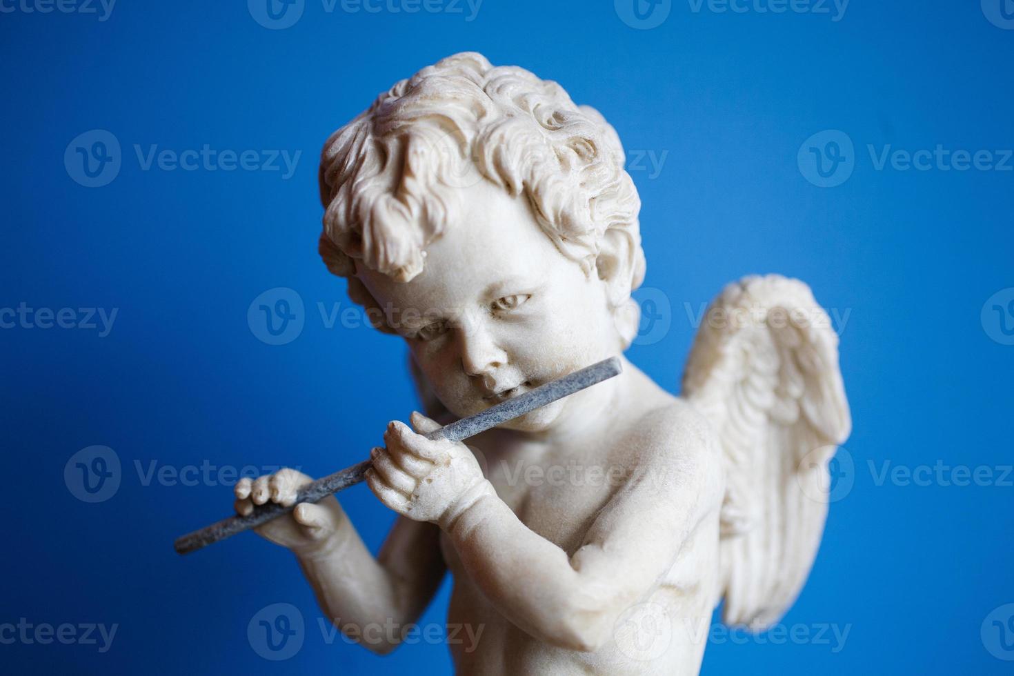 statue of an angel playing the flute on a blue background portrait photo