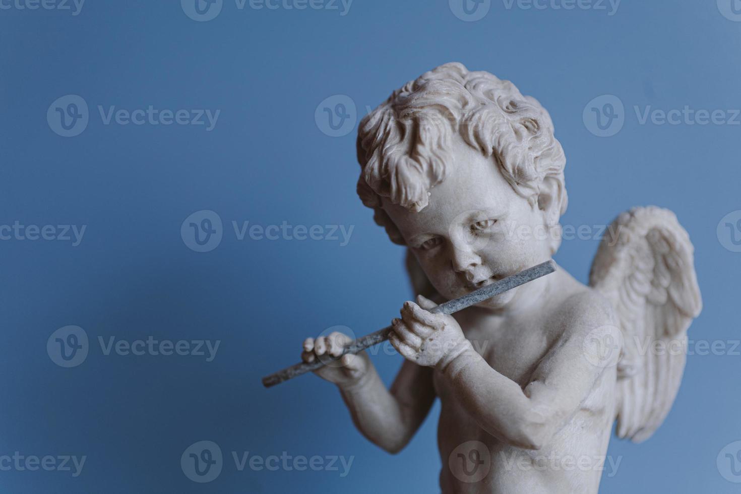 statue of an angel playing the flute on a blue background portrait photo