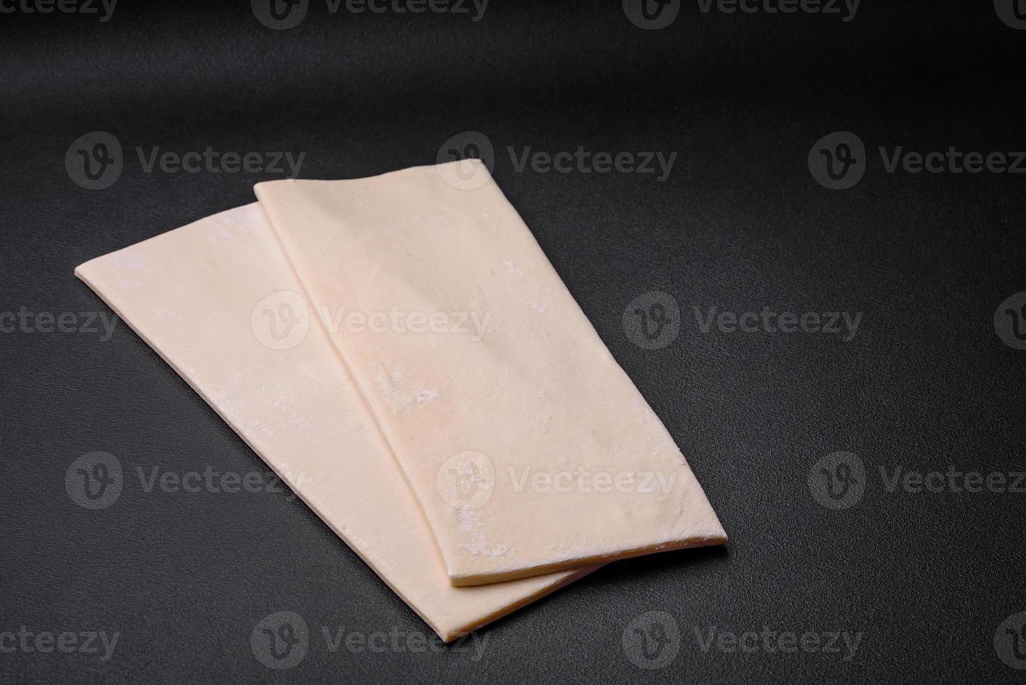 Sheets of raw puff pastry on a dark concrete background photo