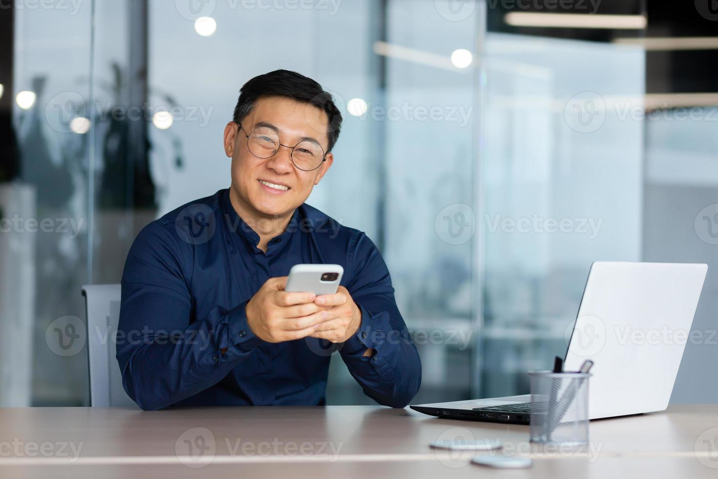 Phone, thinking and man by office window for career inspiration, job search  or online networking. Contemplating asian person or young entrepreneur  cellphone, smartphone or mobile app in workplace Stock Photo