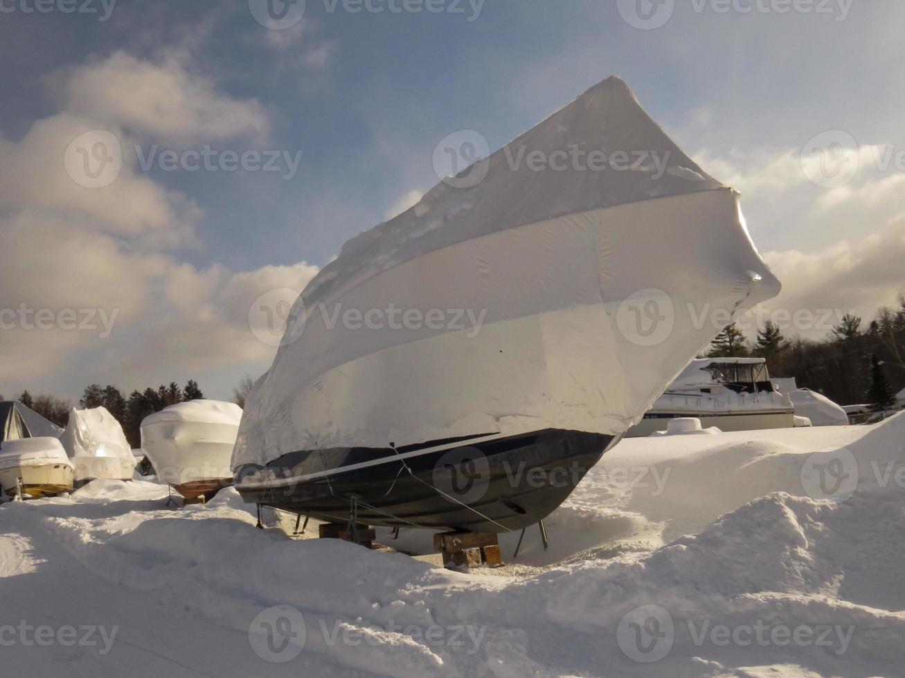 Boat sitting on blocks covered in shrinkwrap with other boats and snow photo