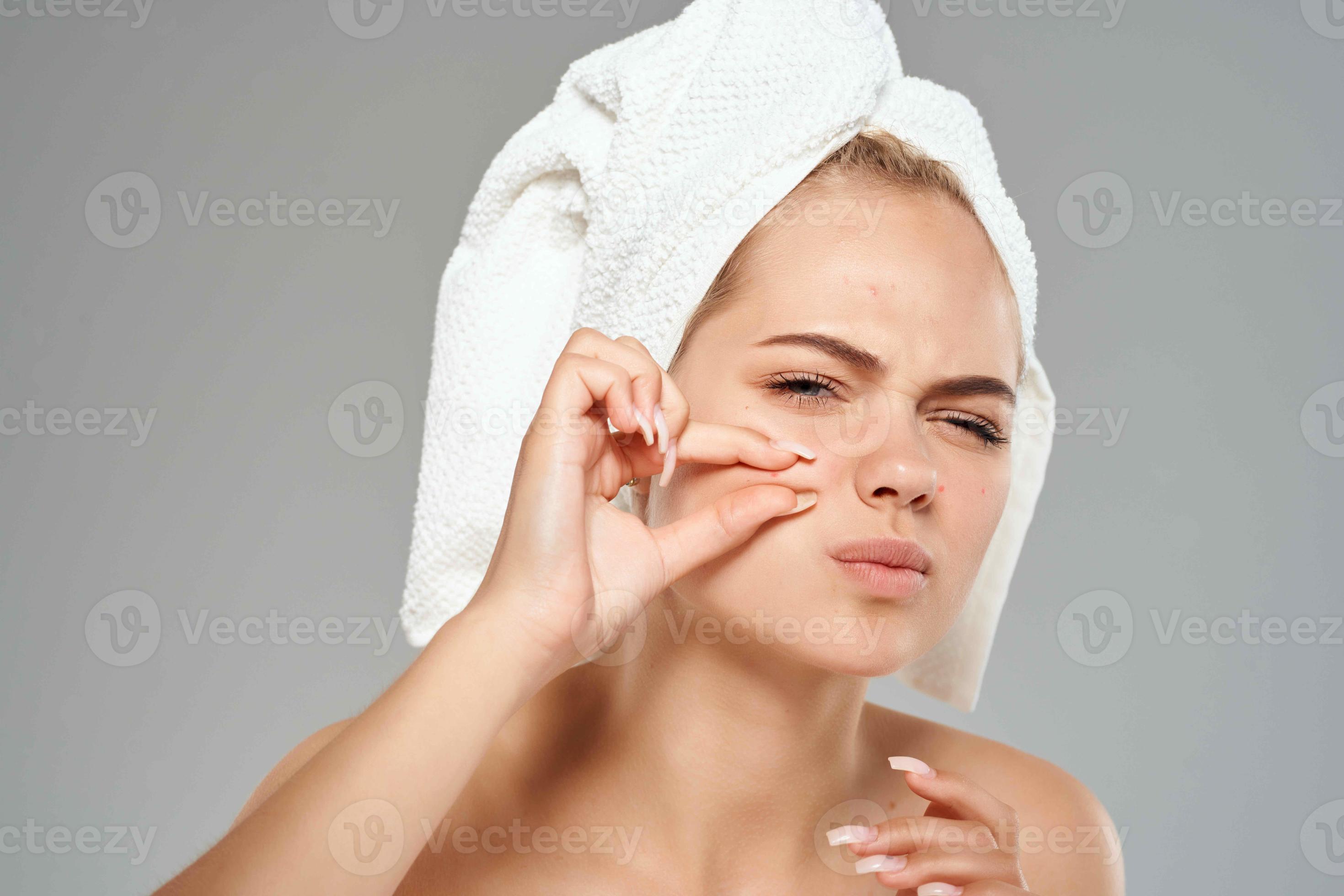woman with bare shoulders squeeze pimples on her face towel on her head