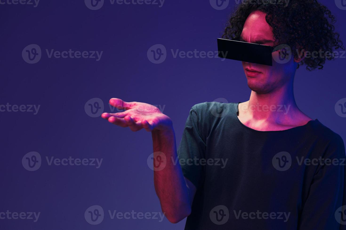 Excited stylish tanned curly man in black t-shirt eyewear touches invisible object posing isolated on color pink blue background. Cool fashion offer. Virtual Reality New Collection concept. Copy space photo