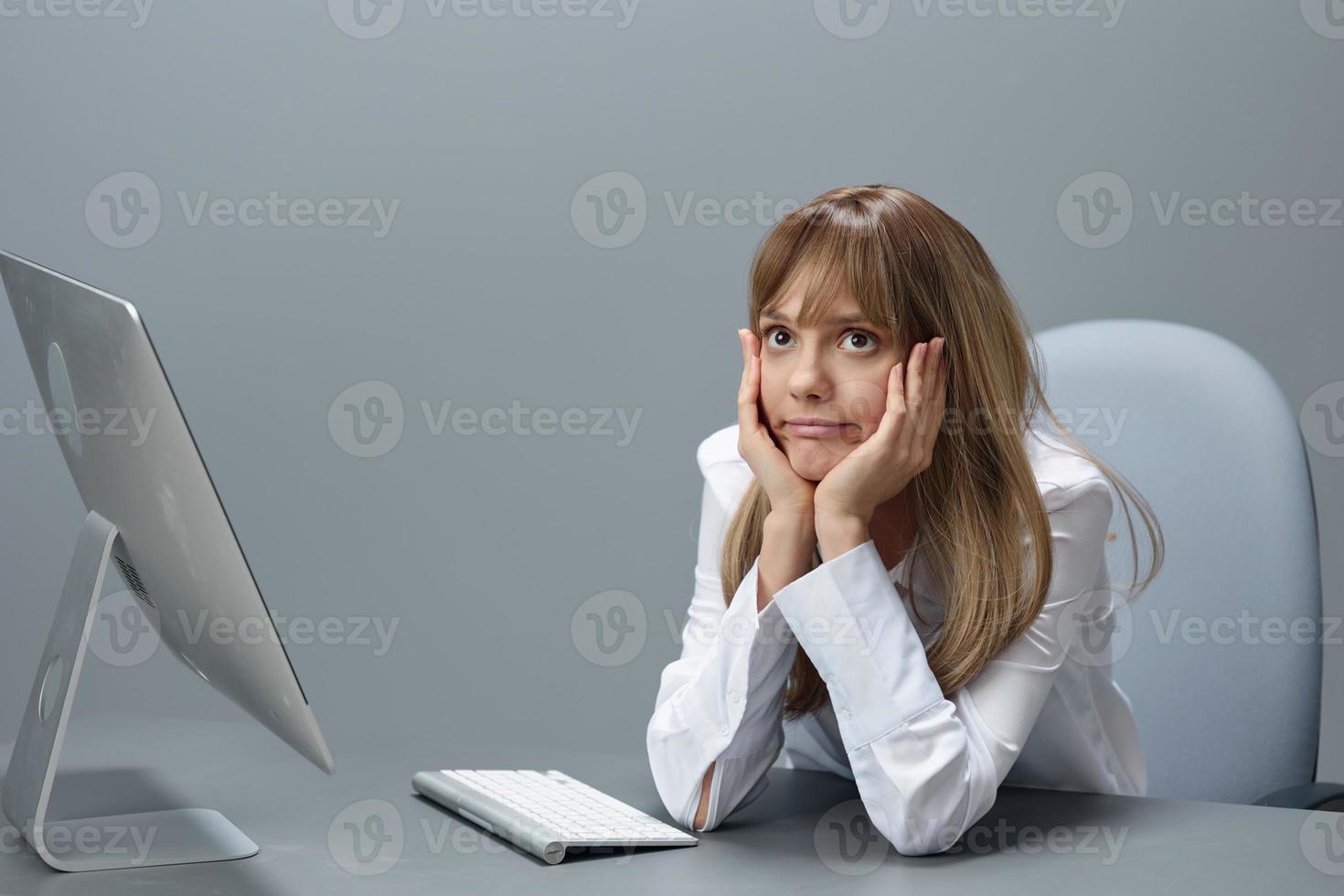 Bored pretty blonde businesswoman worker freelancer using desktop computer sitting at workplace in gray modern office. Remote Job, Technology And Career Profession Concept. Copy space photo